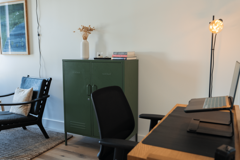 Green storage cabinet with a wooden desk and black rolling office chair.