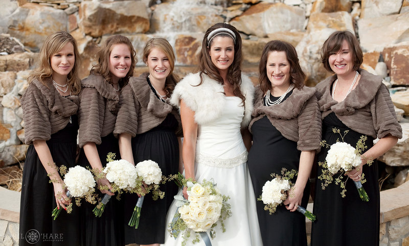 A winter bride wearing a headband and fur shawl photographed with her bridesmaids in front of the outdoor fountain at Cielo at Castle Pines
