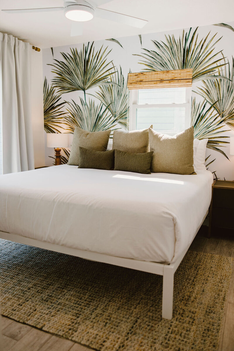 bedroom with palm wallpaper, green pillows, and white linen