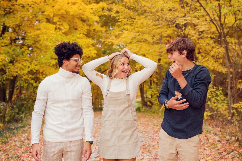 Three teenagers are laughing hard in the yellow fall leaves in Indiana.