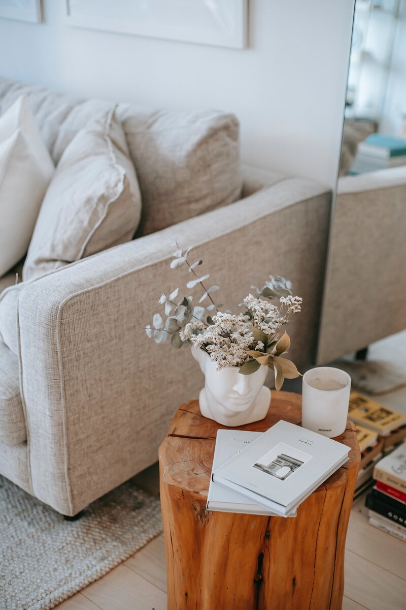 statue head vase with flowers on a side table with a books and a cup