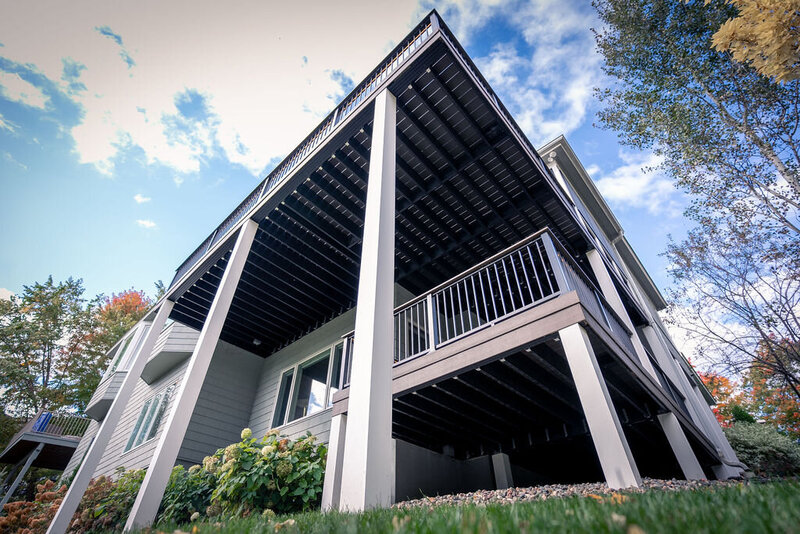 Low-angle view of two low-maintenance decks on a suburban house with substantial white PVC-wrapped posts. 