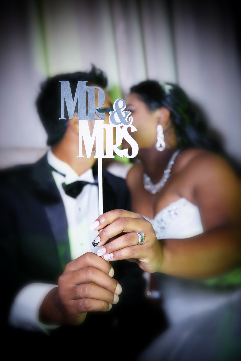 A couple kisses behind a "Mr&Mrs" photo booth prop. Photo by Ross Photography, Trinidad, W.I.