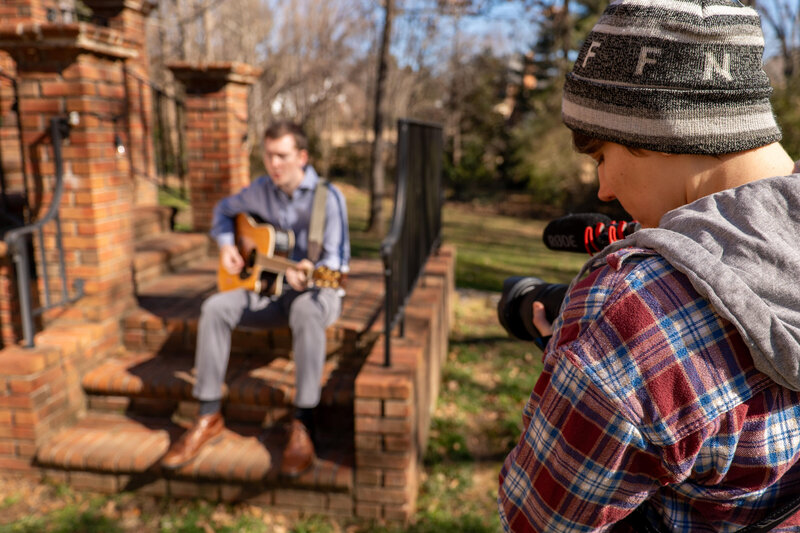 A videographer recording someone sitting on steps playing guitar 