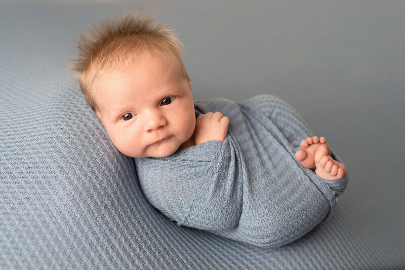 Newborn Baby boy swaddled at looking at the camera at newborn session.
