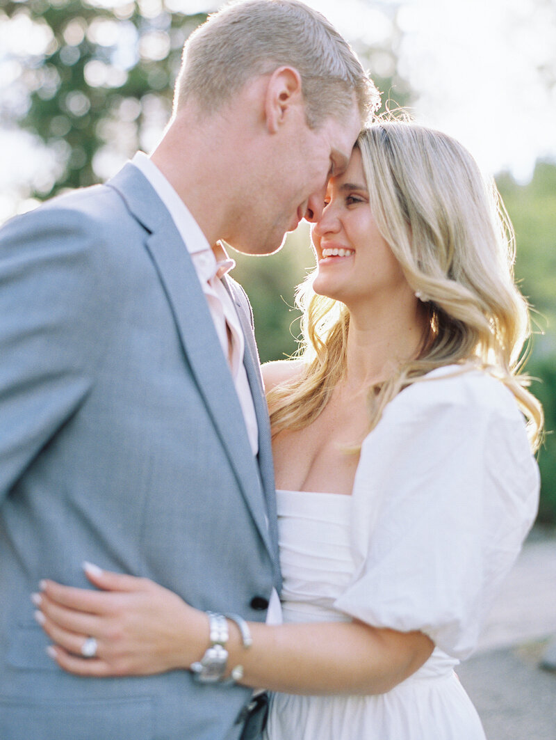 Close up of couple in the sunshine wearing a white  puff sleeve dress and  a grey suit smiling at each other