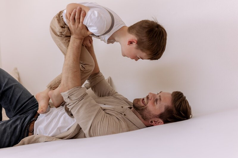 Vater liegt auf dem Ruecken und haelt seinen Sohn ueber sich