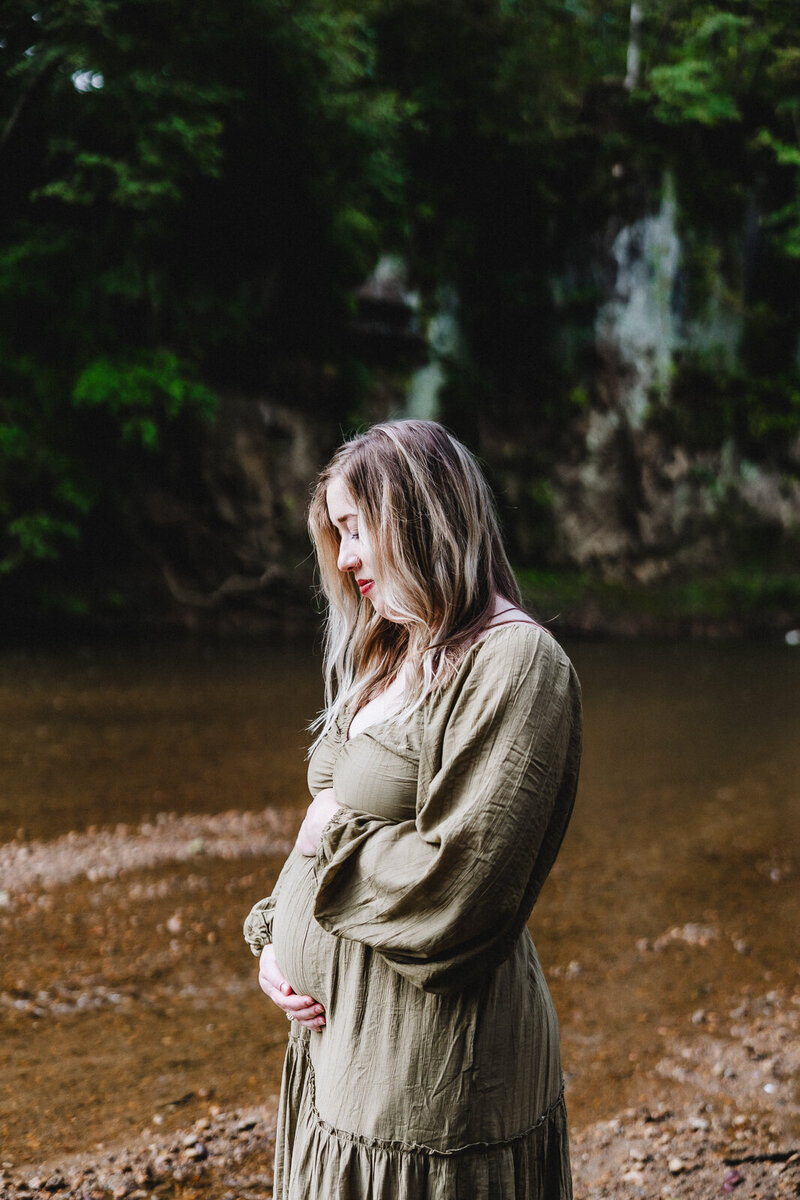 Maternity photo of pregnant woman holding belly with both hands, looking down peacefully