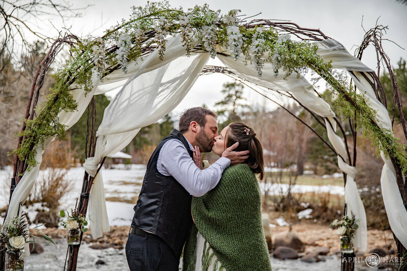 Wedding Kiss Under Arch Next to River at Romantic Riversong Inn Estes Park CO