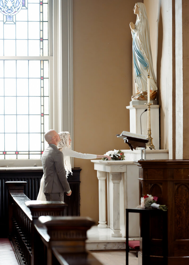a catholic bride and groom present flowers to Mary, asking for her intercession during their catholic wedding Mass at St. Mary's in downtown Nashville, Tennessee