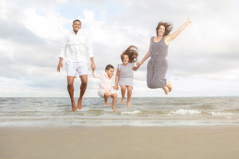 fun beach portrait of a family of four jumping up with the Atlantic ocean behind them