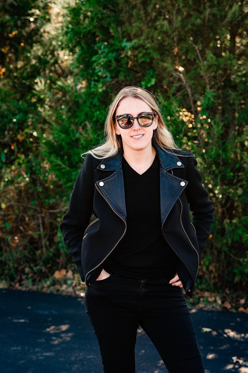 Social Influencer wearing all black with jean jacket and bold sunglasses smiling at camera