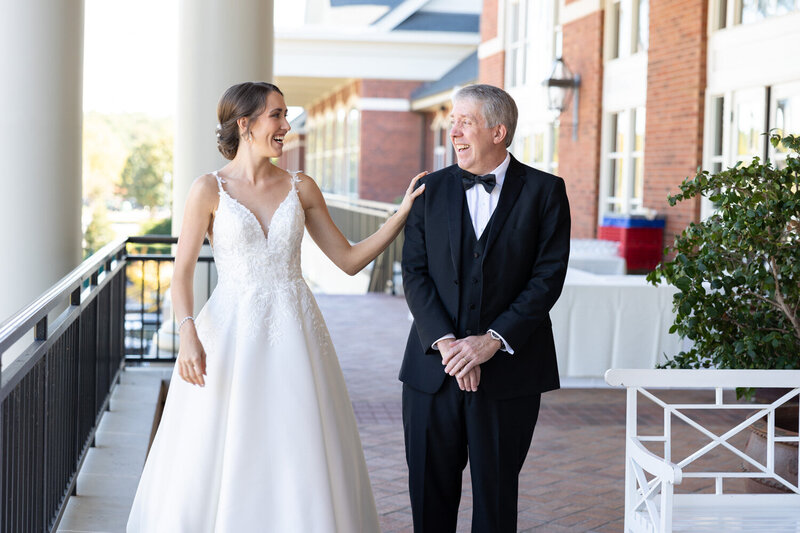 Bride in plunging neck line wedding dress with lace detail around neck line doing a first look with her father in a black tux with a bow tie at prestonwood country club