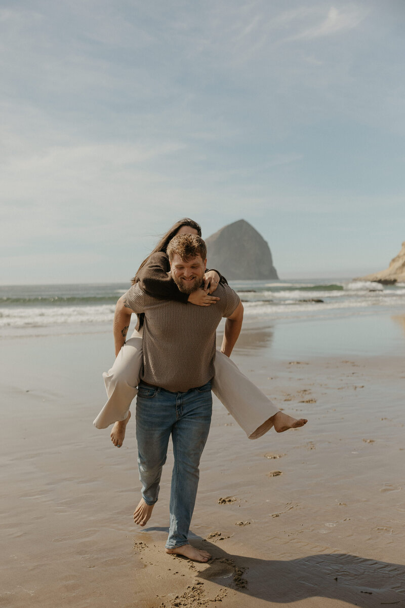 A person walking on a beach with their partner on their back 