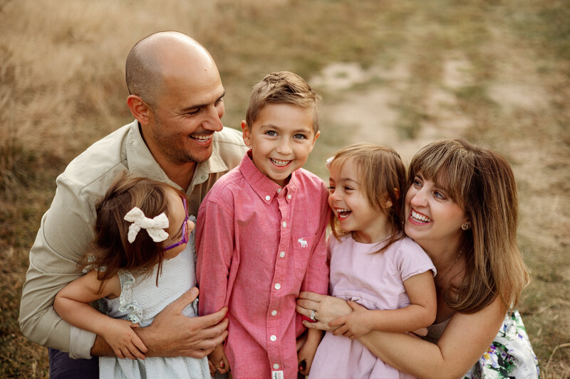  A fun and loving family of four laughing together in an outdoor setting in Grand Rapids, Michigan, during a relaxed and natural family photography session.