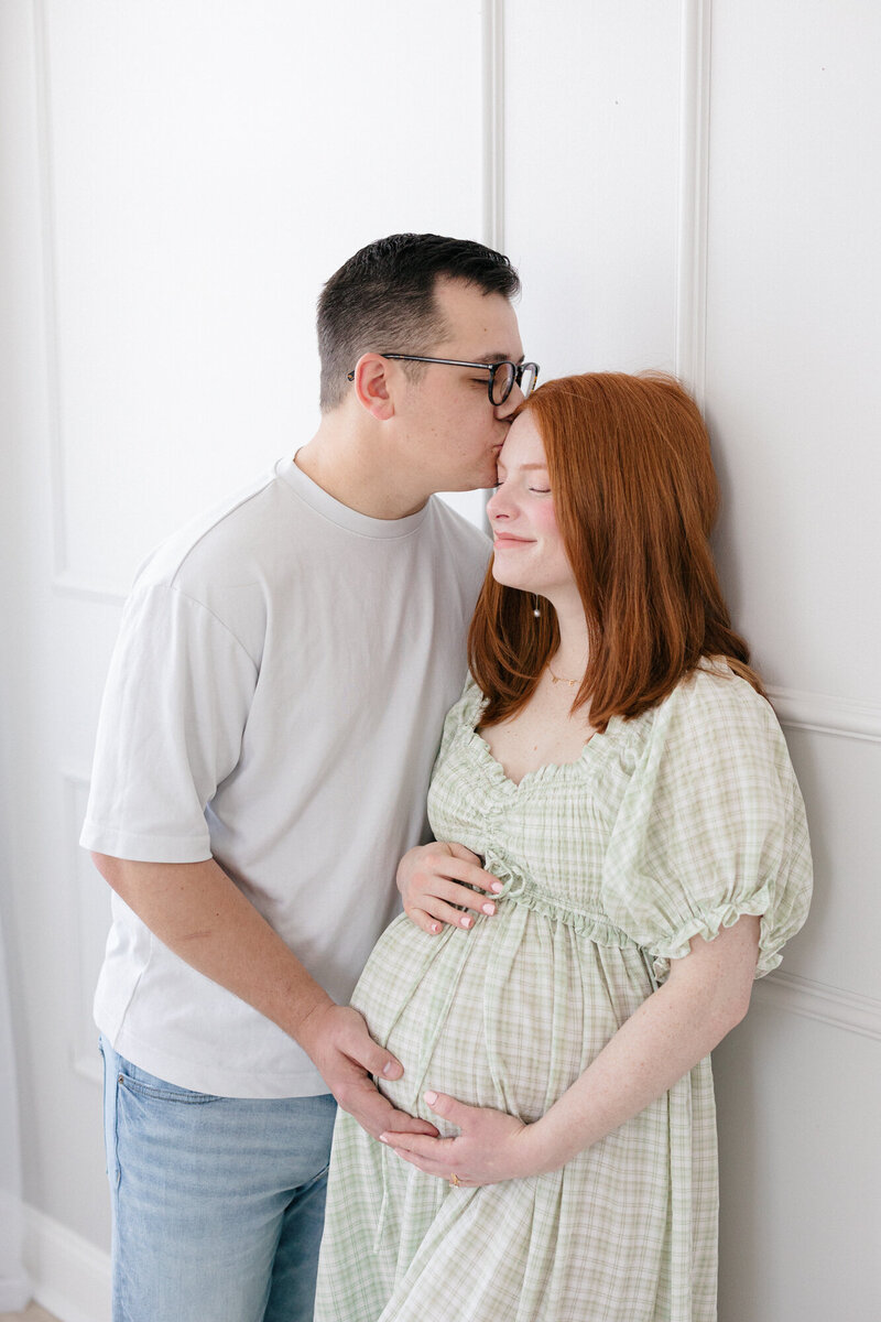 Expecting parents leaning against a wall in a louisivlle maternity photography studio