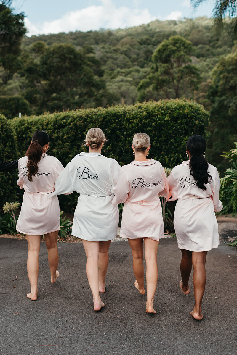 Bride Kristen walking  with her bridesmaids  in satin wedding day gowns with their hair and makeup done.