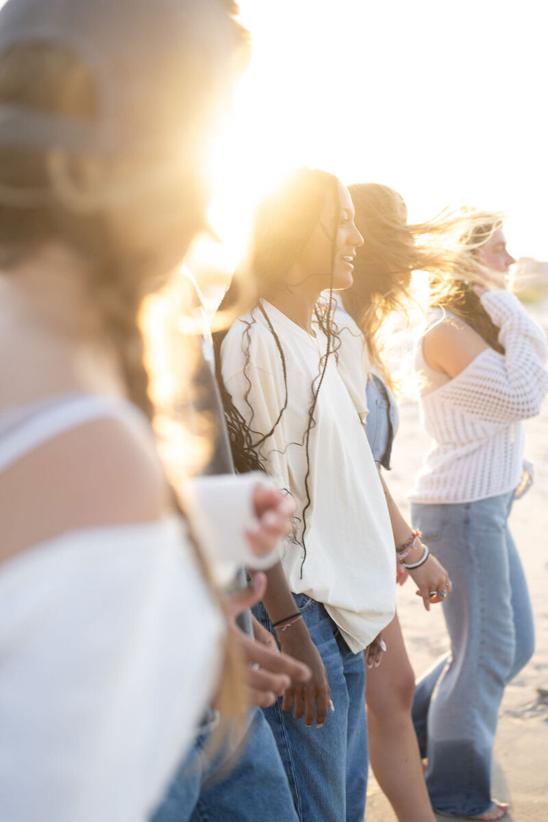 a group of five friends walk on the beach during golden hour laughing and holding coffee and tea from sundial in surf city, north carolina