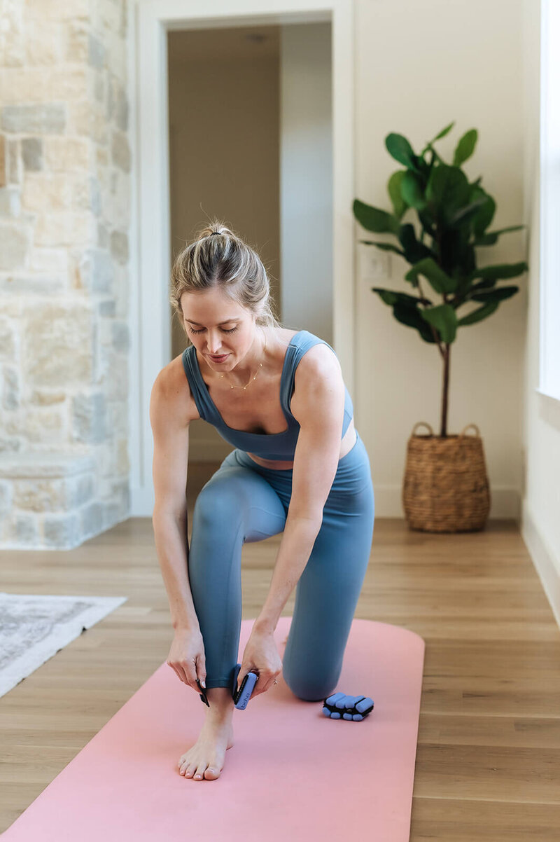 Erica Taylor adjusting ankle weights on a yoga mat—showing simple, realistic movement routines for busy moms
