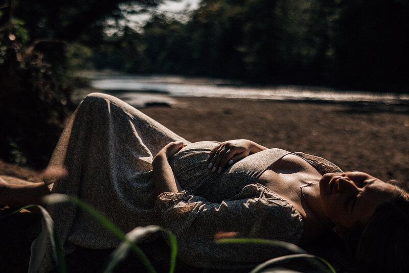 Maternity portrait of expecting mother laying on a log at sunset with deep shadows and a dramatic look. 