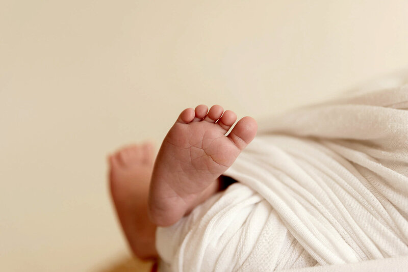 Close up image of newborn baby feet with the newborn wrapped in a white swaddle