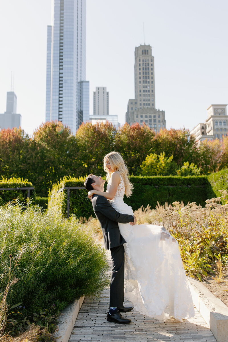 Groom lifts his bride in the air with Chicago skyline behind them