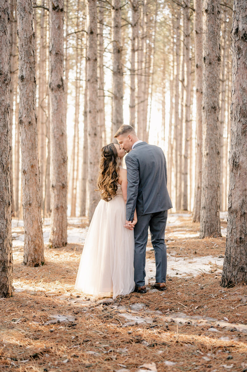 Bride and groom leaning over to kiss each other in the tall pines of Warner Lake County Park in Clearwater Minnesota