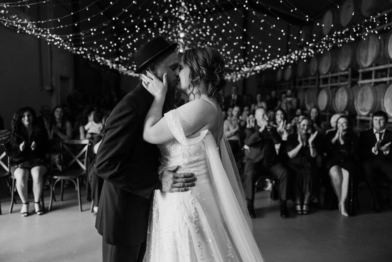 A black and white image of a couple at their micro wedding having their first dance under twinkling lights