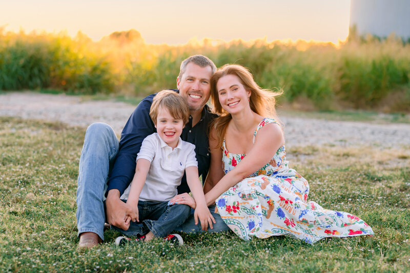 Smiling family sitting together outdoors during a golden hour portrait session in McKinney, Texas, photographed by Jennifer L. Kirk Photography.