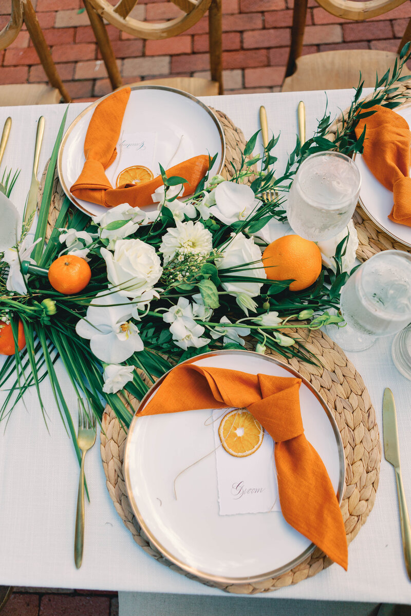 Vibrant citrus-inspired table setting with orange napkins and floral centerpiece.