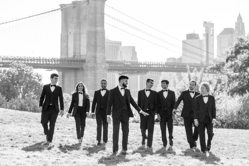 black and white photo of groomsmen walking towards the camera with a bridge in the background