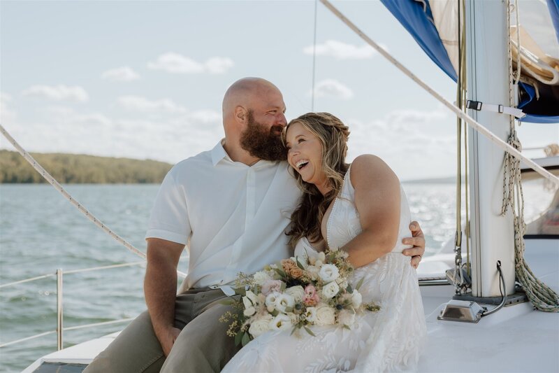 bride and groom laughing together while sitting on the deck of a sailboat