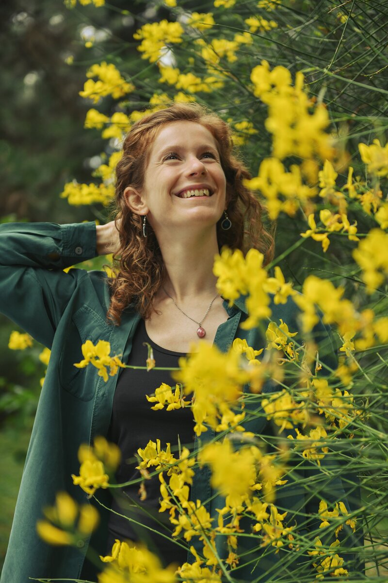 Une femme épanouie et souriante est entourée de fleurs sauvages jaunes. Elle fait de la méditation de pleine conscience