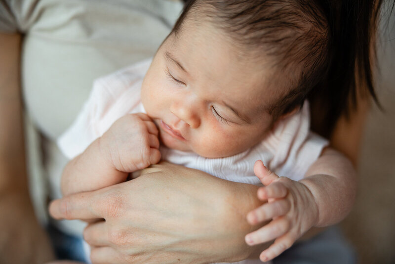 A newborn being held in her mother's arms asleep.