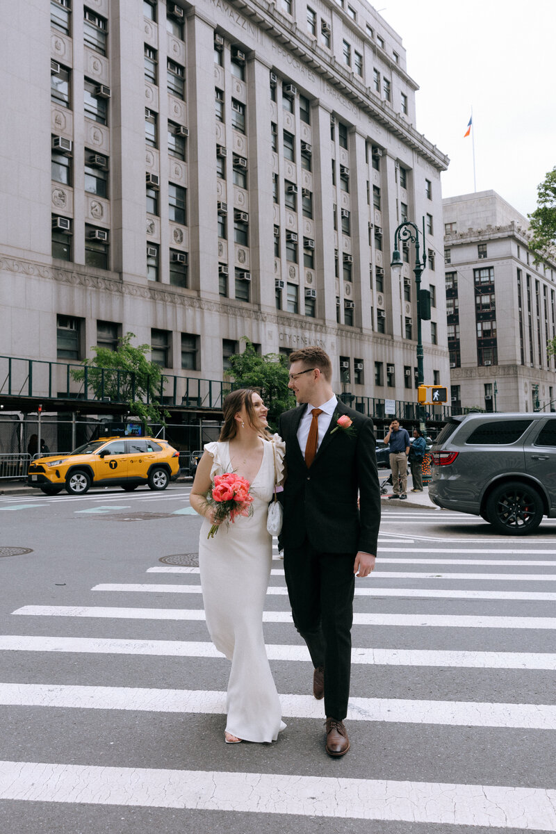 Engaged couple holding hands while crossing the street near Manhattan City Hall during their NYC elopement