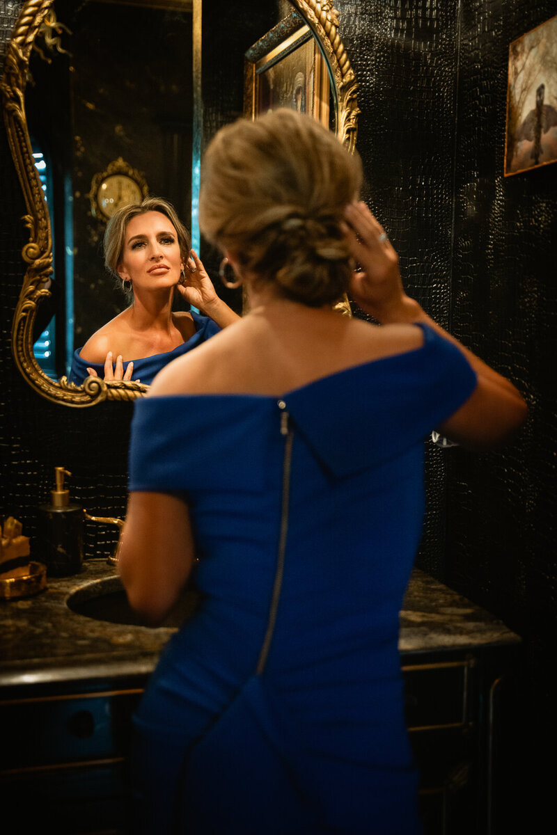Lady in blue dress all glam up looking at her self in the mirror