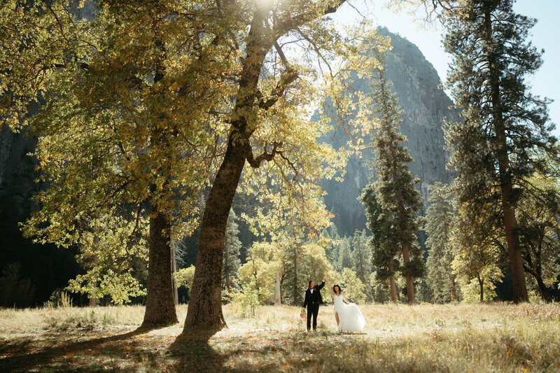 Couple walk along a path in a green meadow surrounded by granite formations, the perfect place for a yosemite wedding