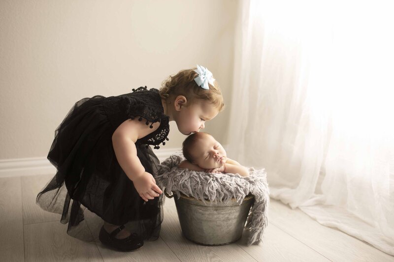 Big sister kissing newborn brother in studio with Heather Bush