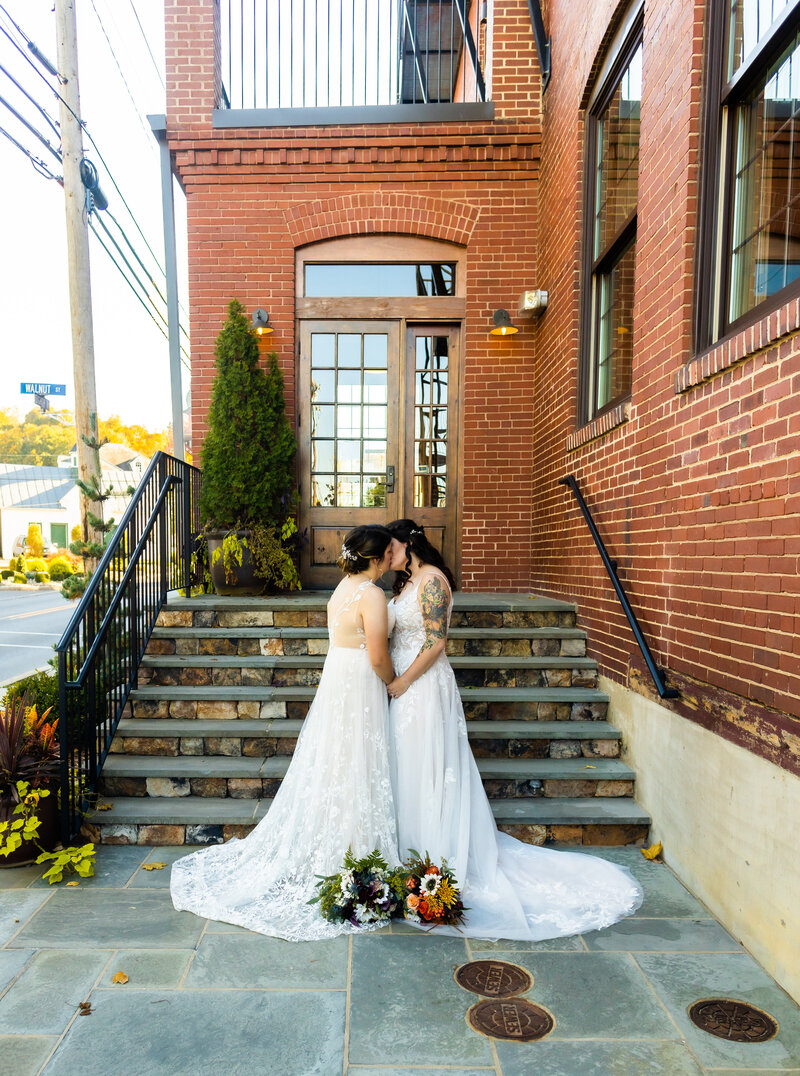 Brides embrace in a kiss near the stairway at Rusty Rail Brewery, PA Wedding Photography