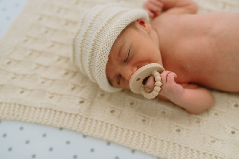 baby in a cream hat with a cream pacifier laying on a cream blanket