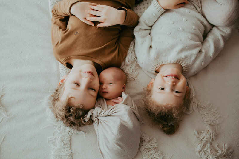 Trois petits enfants, un garçon de 6 ans, une petite fille de 3 ans et un bébé, tous les 3 allongés sur un lit, l'un sourit, l'autre ferme les yeux, l'autre regard vers l'horizon, le bébé est positionné dans  le sens inverse des 2 autres et au milieu. Ce sont mes enfants !