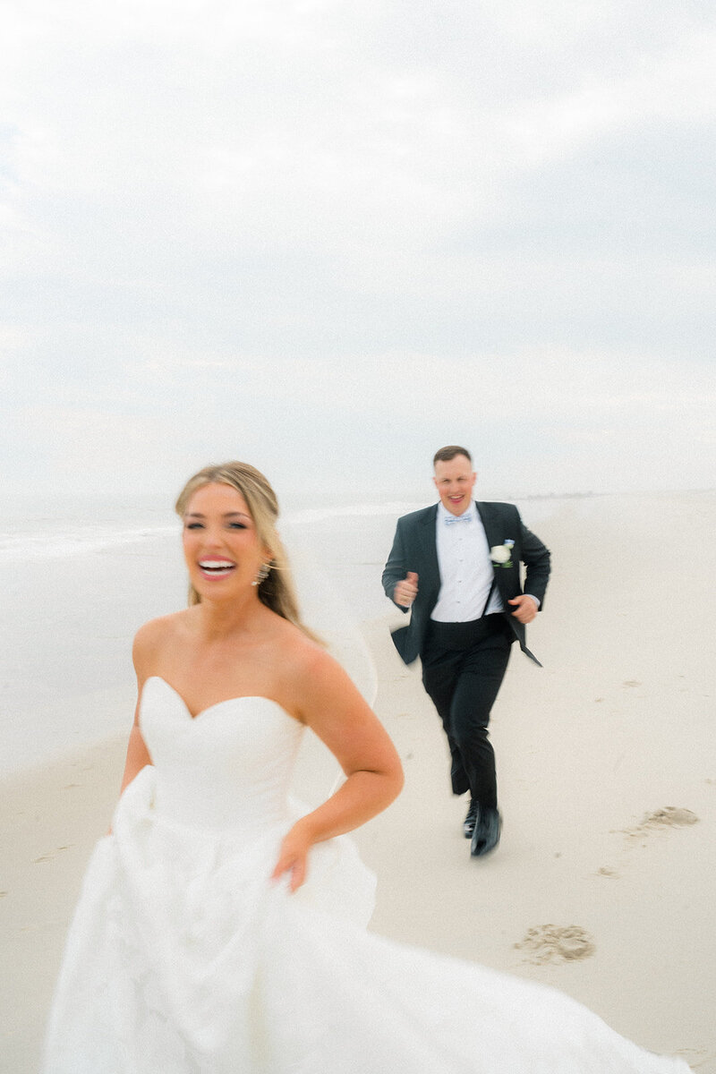 A bride and groom running and laughing on a beach in New Jersey.