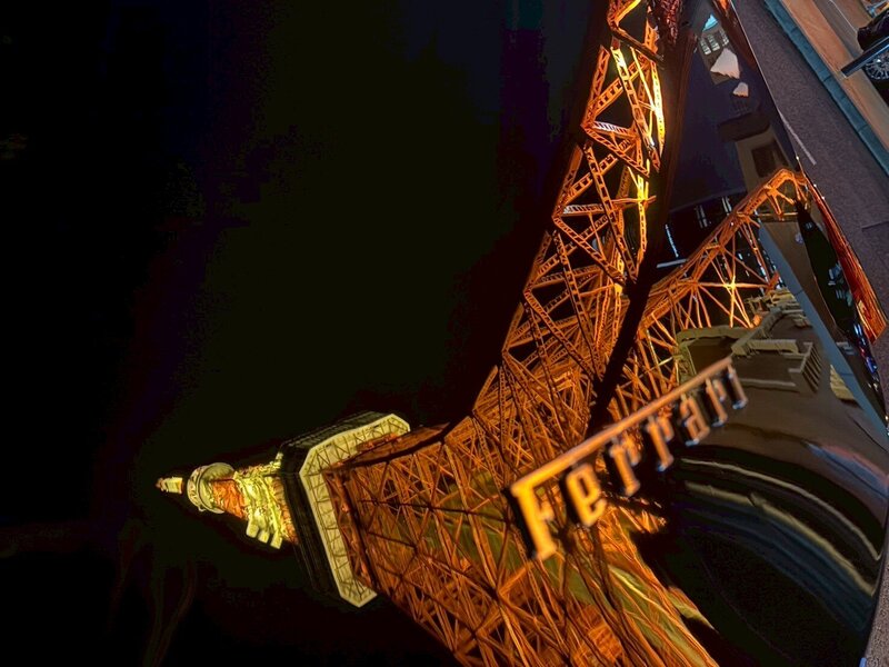A creative night shot capturing Tokyo Tower reflected on the hood of a Ferrari, with the Ferrari logo prominently visible.