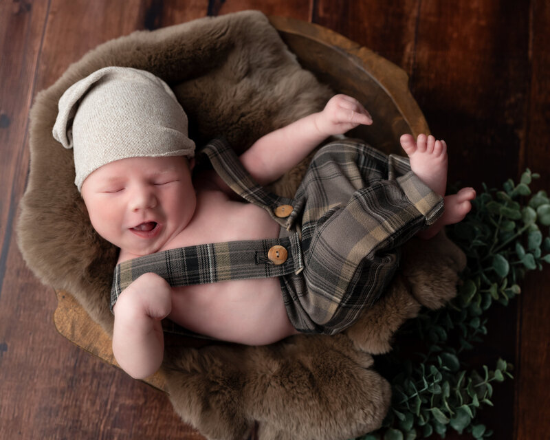 Smiling newborn in plaid overalls and soft brown textures, styled in-studio in Paris, Ontario.