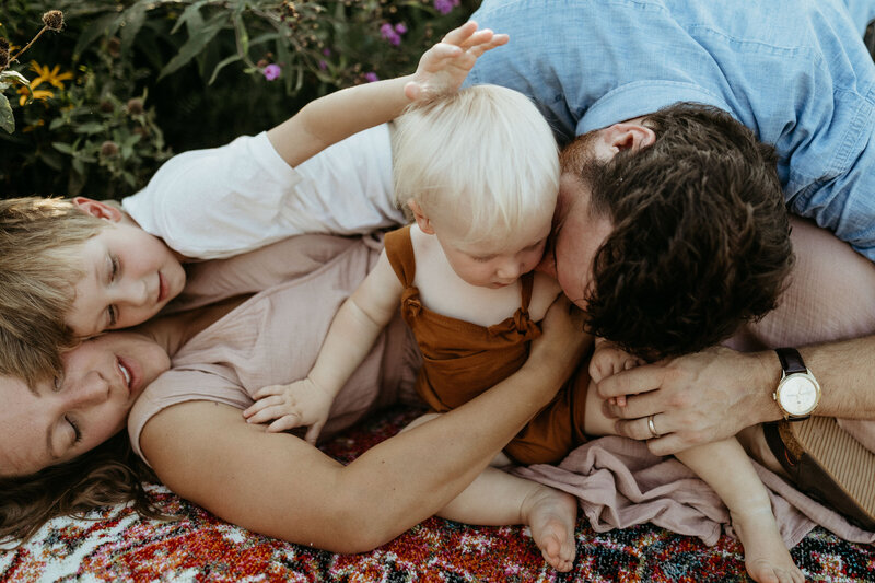 Young family with 2 boys all laying on top of each other on a boho rug