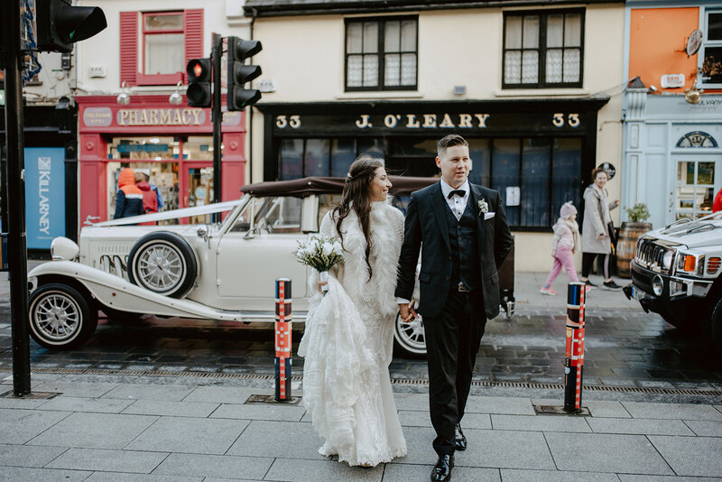 Bride and groom walking in front of J. O'Leary antique shop on Main Street in Killarney, Ireland