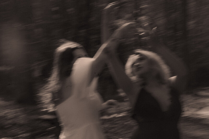 Two brides dance together by a creek with a slow shutter speed.