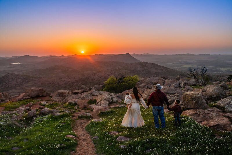 A cinematic family portrait at sunset in the Wichita Mountains, capturing a heartfelt moment of connection and wonder as they gaze toward the glowing horizon.