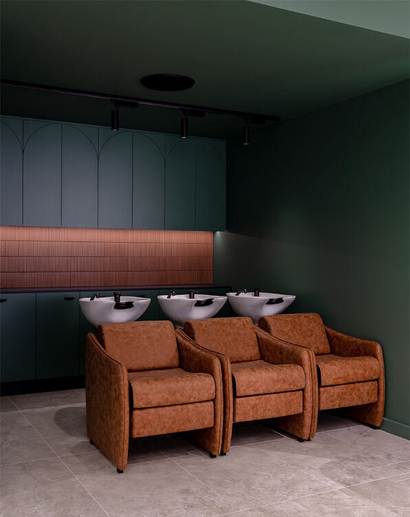 Luxurious hair washing station with three leather chairs and modern basins against a green and wood-accented wall, offering premium hair treatments in Sydney.