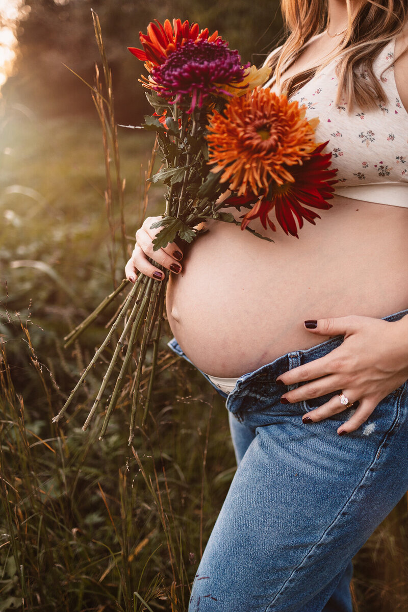Close up image of an expecting mother's belly with flowers and blue jeans. 